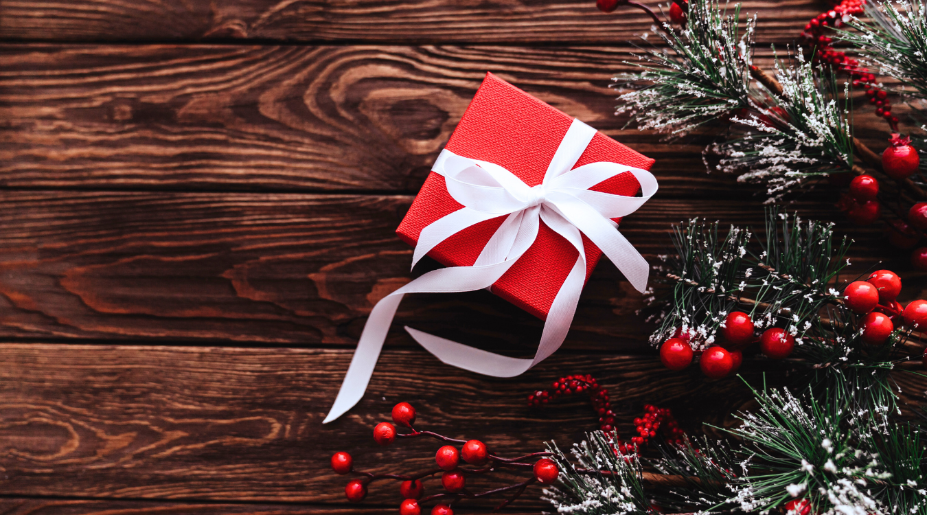 A red christmas gift next to pine branches and berries on wood.