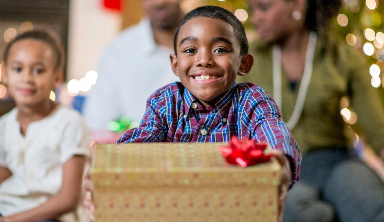A little boy smiling big as he holds a gift box in his hands