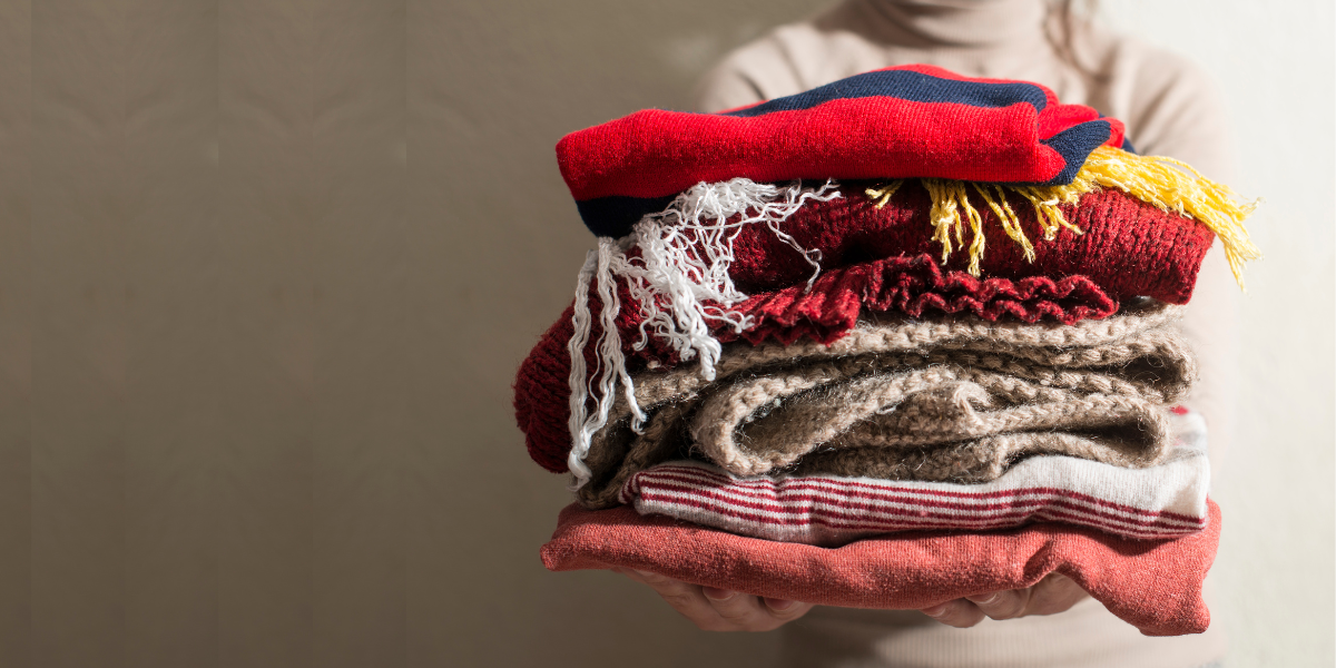 Someone holding a bunch of folded winter clothing like scarves and sweaters